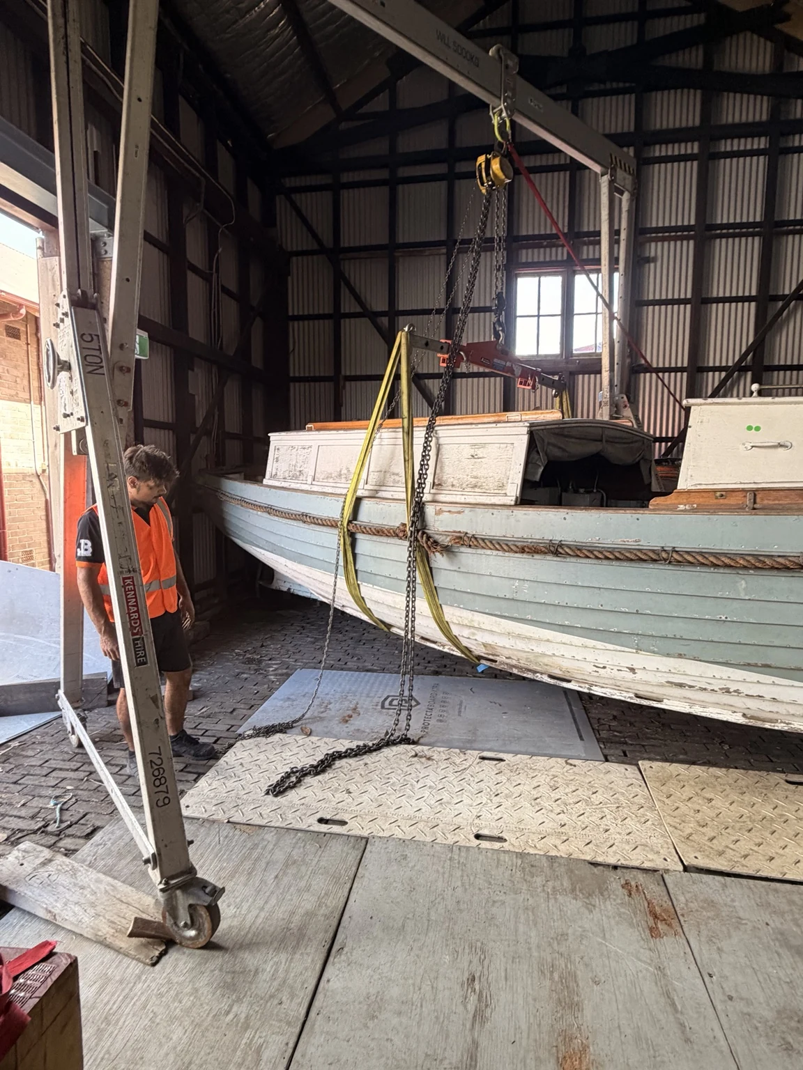 JB crew member beside the boat supported by slings beneath a gantry inside the Gold Coast heritage building