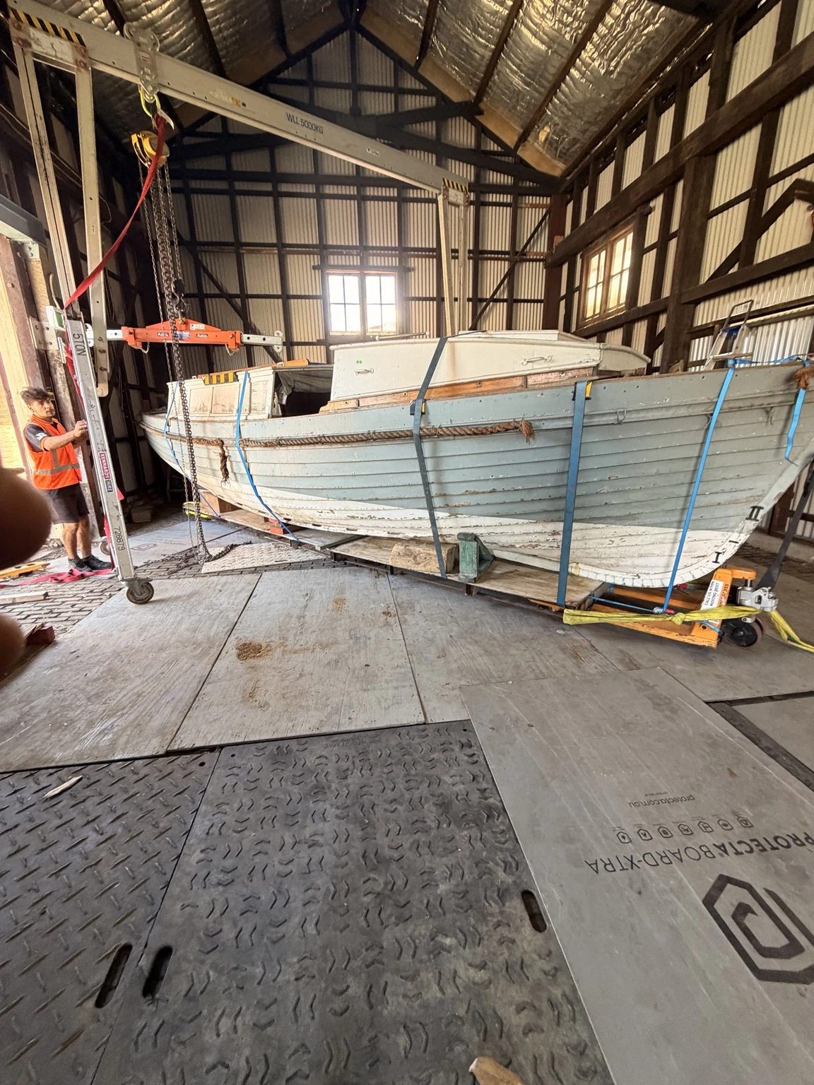 Wide view of the boat, crew, lifting equipment and floor-protection sheets inside the heritage building.