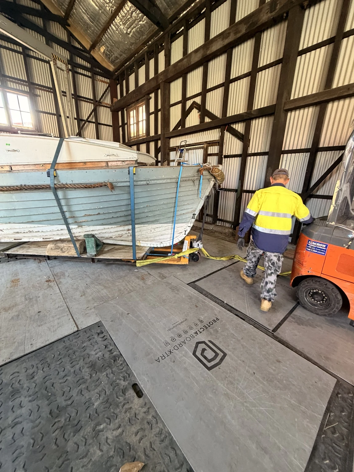 Boat hull with slings, supports and floor protection visible during the move.