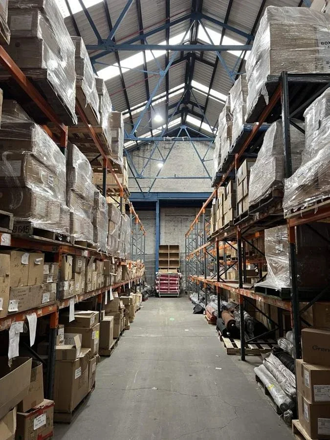 Warehouse aisle with racked cartons and shrink-wrapped pallets at the 3M relocation site
